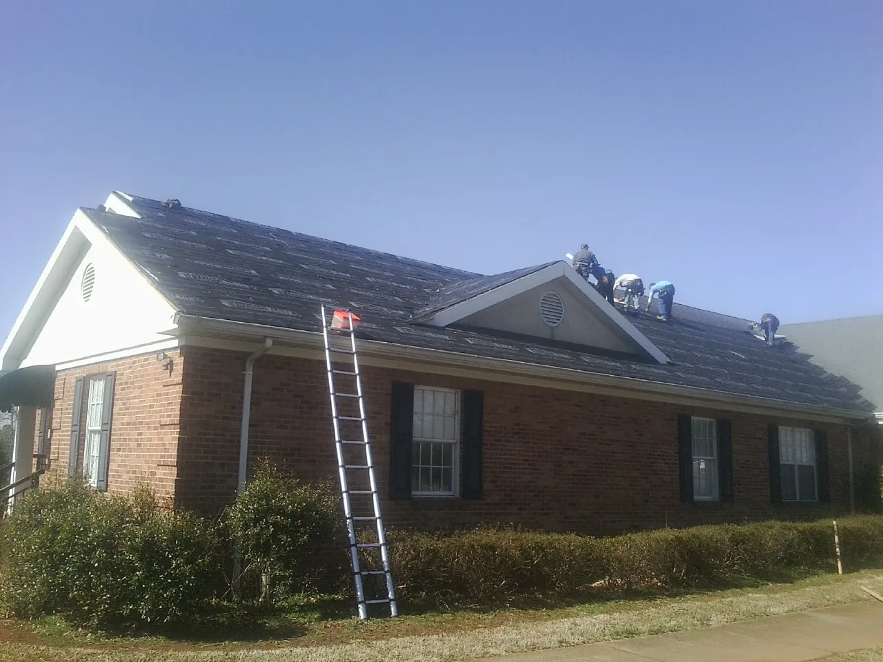 Crew tearing shingles off a brick ranch roof with a ladder set — Emergency Roof Repair work by our crew in Hibernia