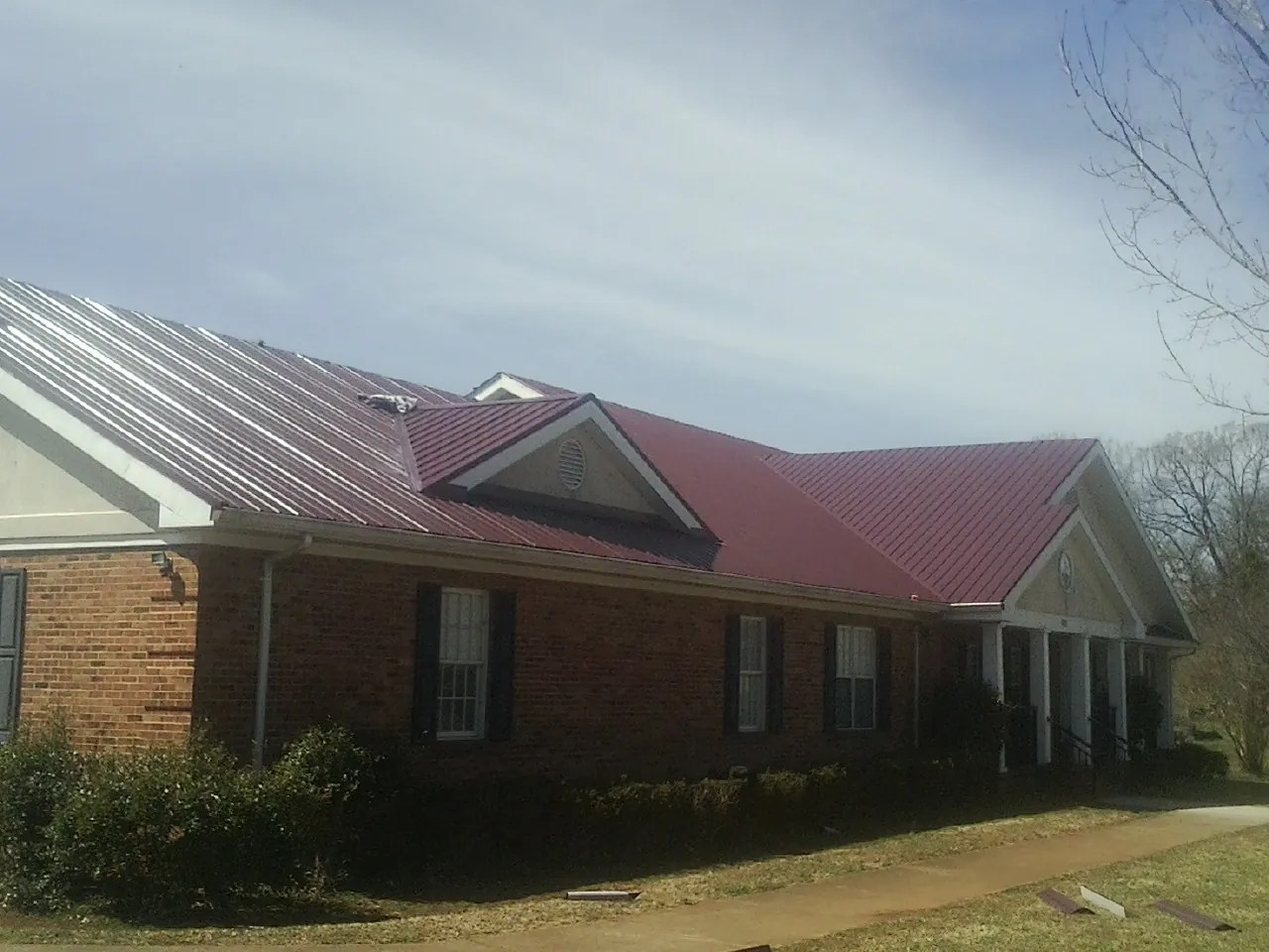 Red metal roof with gabled entries on a long brick building, from a Hail Damage Roof Repair job in Hibernia
