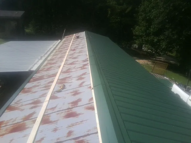 Old rusted panels beside newly installed green metal roofing — Wind Damage Roof Repair by Roofing Brothers in Hibernia