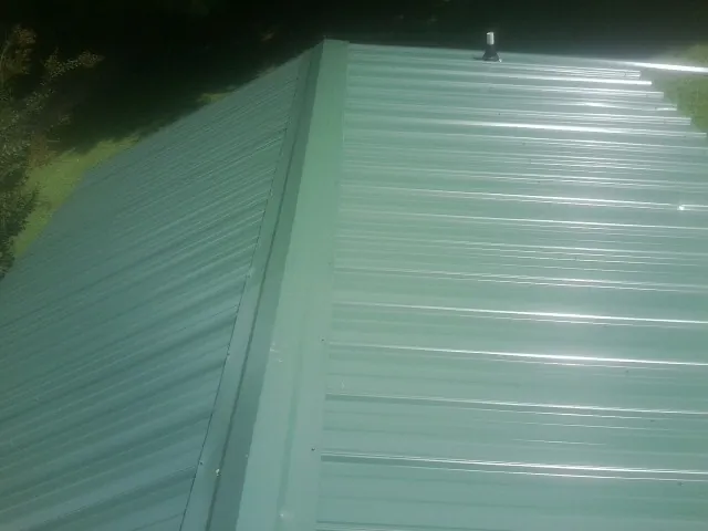 New green metal panels meeting at the ridge of a roof — Flat Roof Repair work by our crew in Hibernia