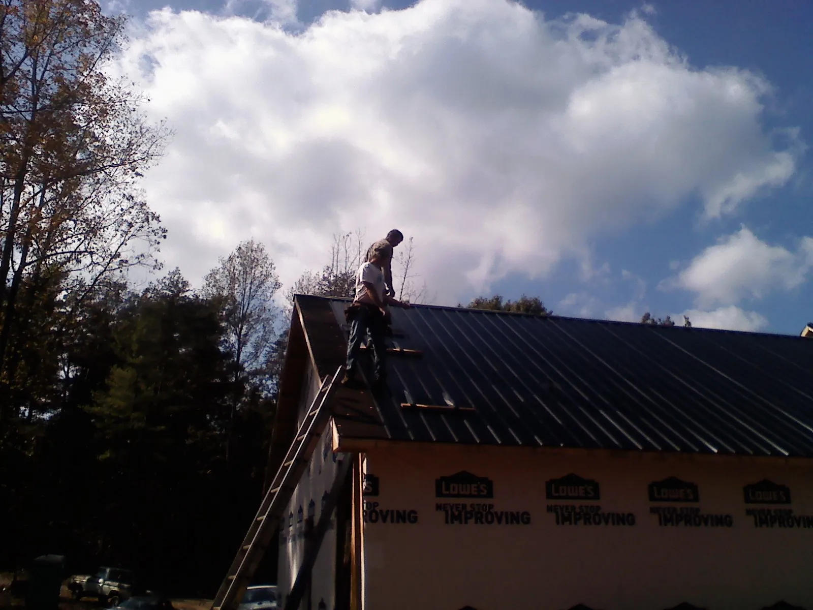 Roofer fastening dark metal panels high against a cloudy sky, from a Roof Inspection job in Hibernia