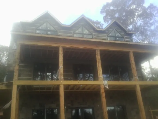 Dormers and porch framing on a large log home under construction — Roof Coating work by our crew in Hibernia