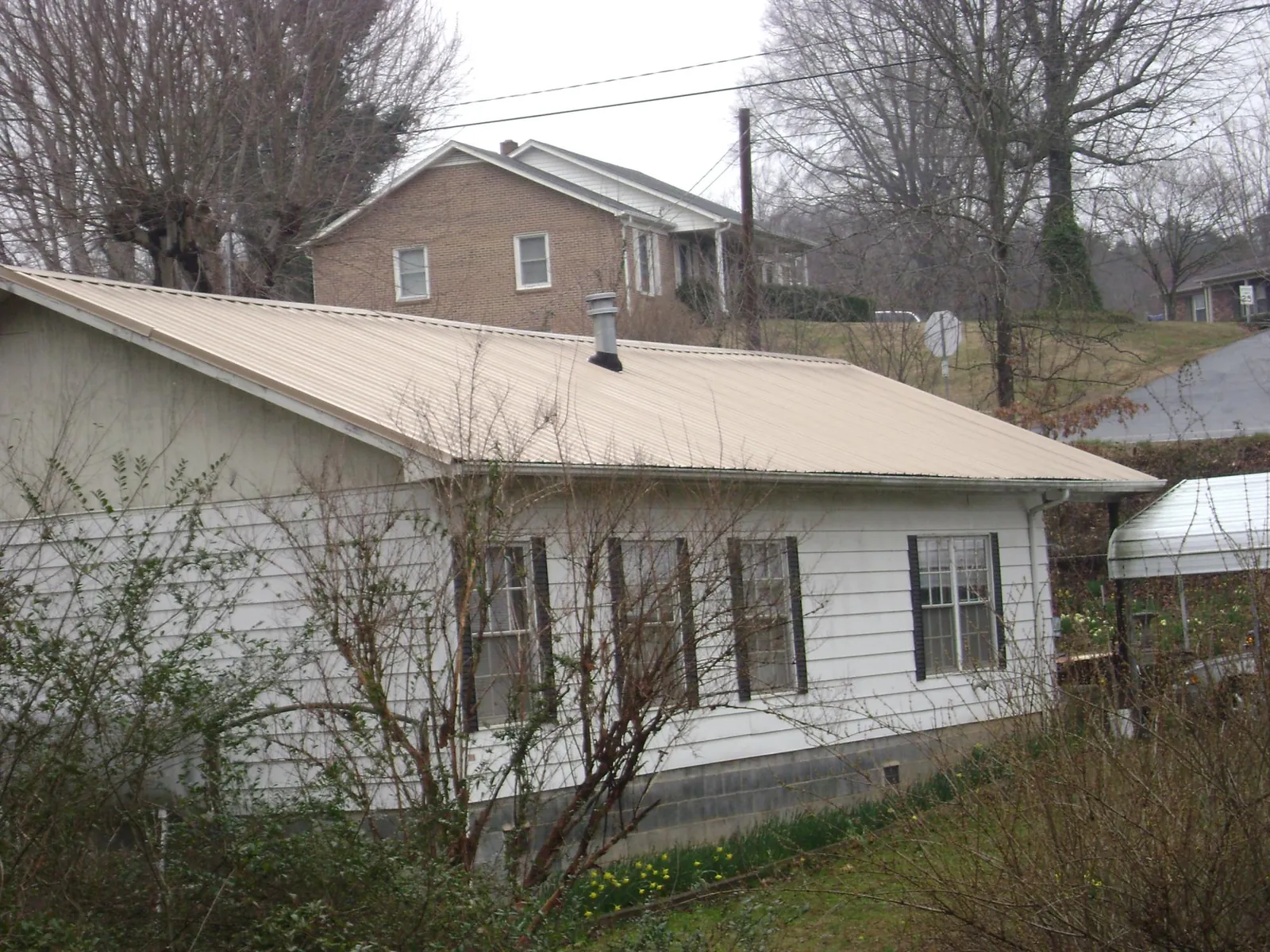 Tan metal roof on a white sided house set into a hillside — Commercial Roofing by Roofing Brothers in Hibernia