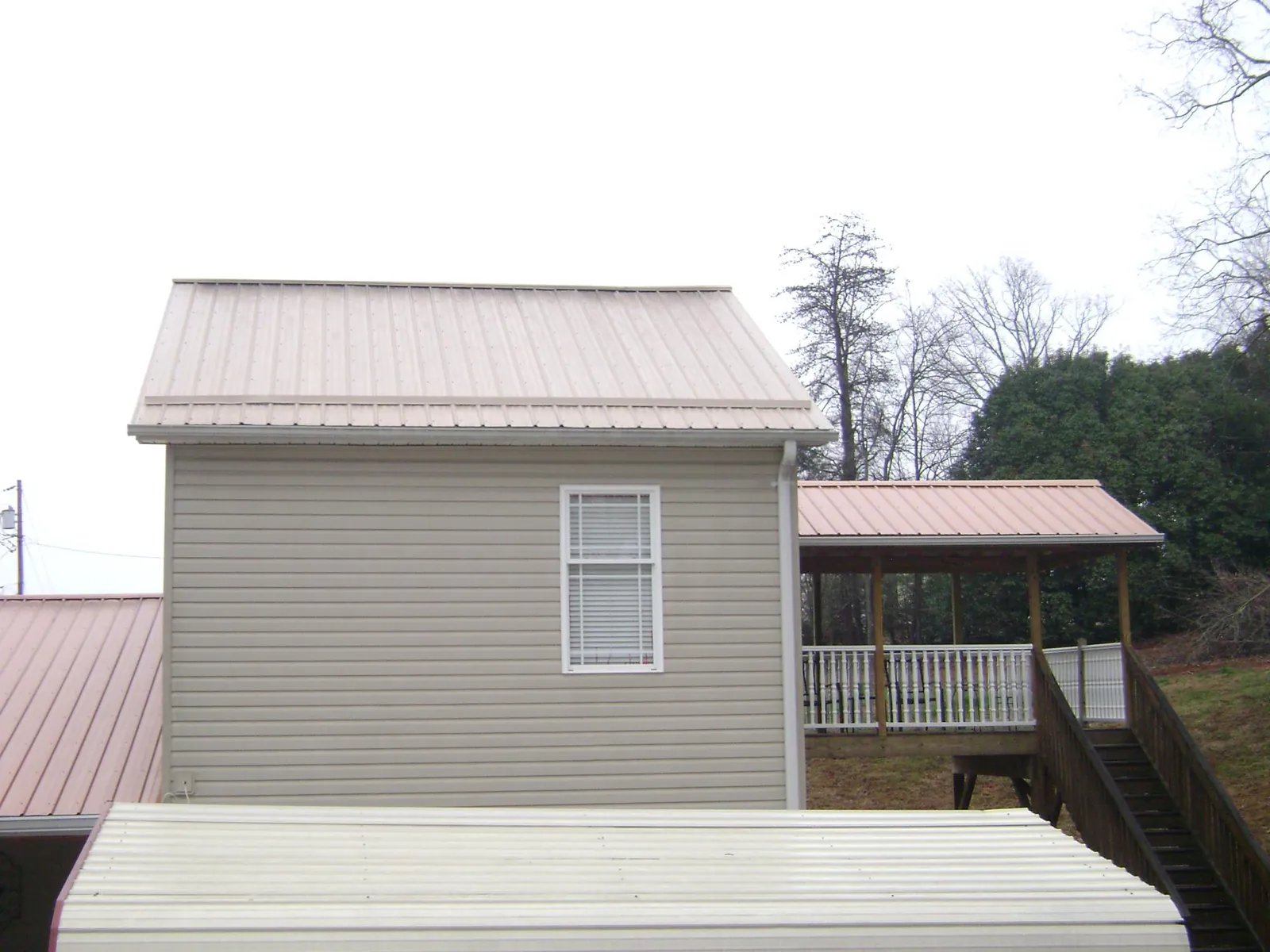 Tan metal roofs on a two story addition and attached porch, from a Roof Replacement job in Hibernia